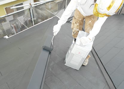 住宅の屋根を専用ブラシで塗装するスタッフ